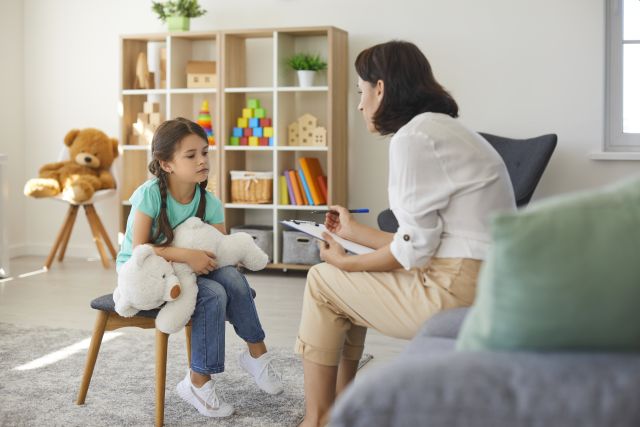 Little girl sharing her concerns with supportive child psychologist during therapy session in